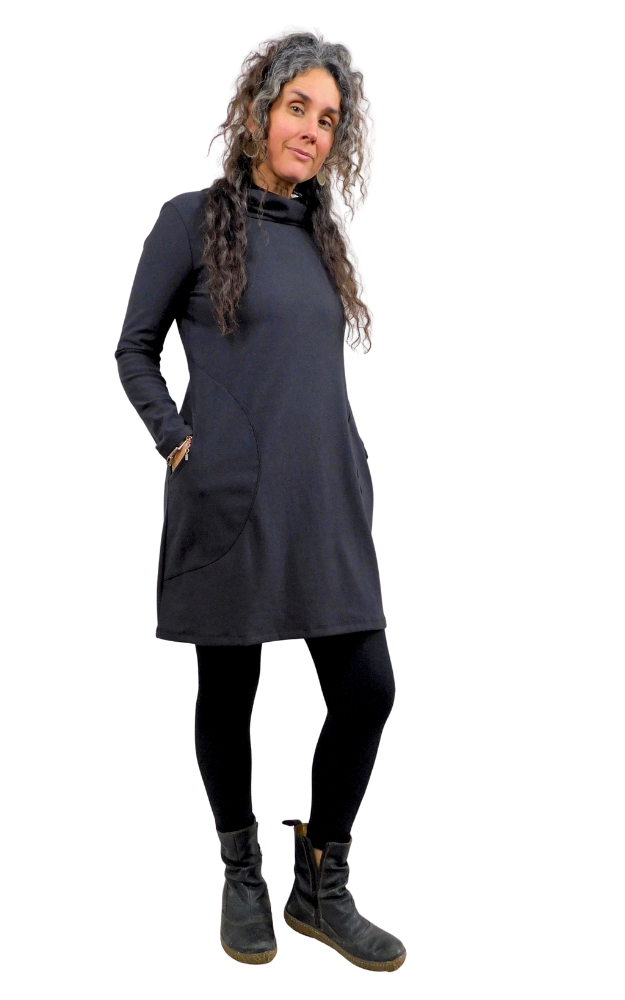 Woman wearing a black tunic dress with hands in pockets on a white background