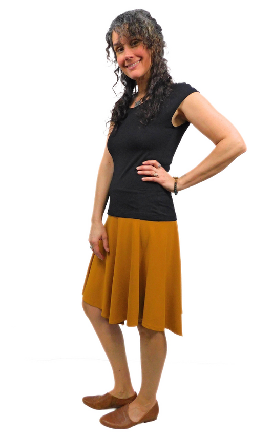 Woman standing in pose hand on hip wearing black top and curry gold skirt
