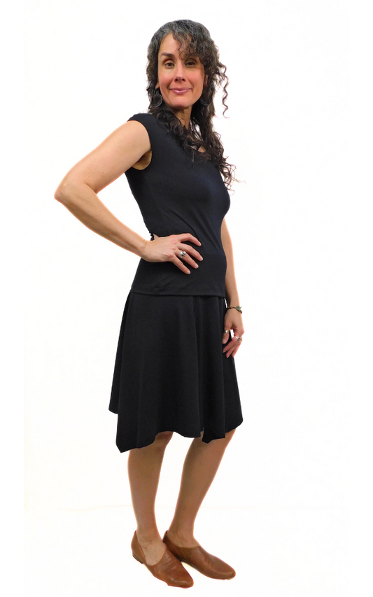 Woman standing in pose one hand on hip wearing black top and black skirt
