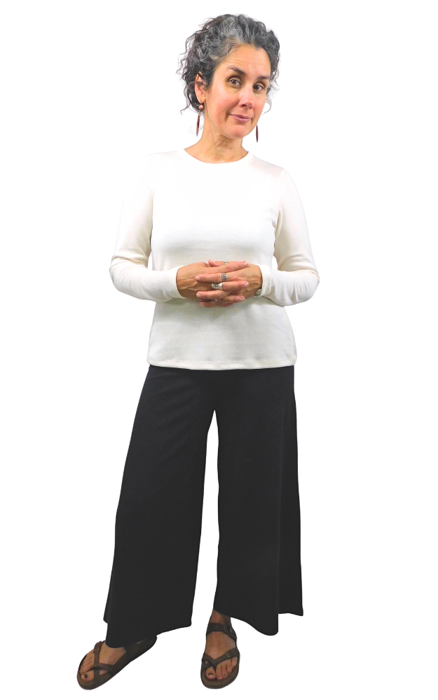 A woman modeling a white long-sleeve crewneck top and black wide-leg pants against a plain white background.