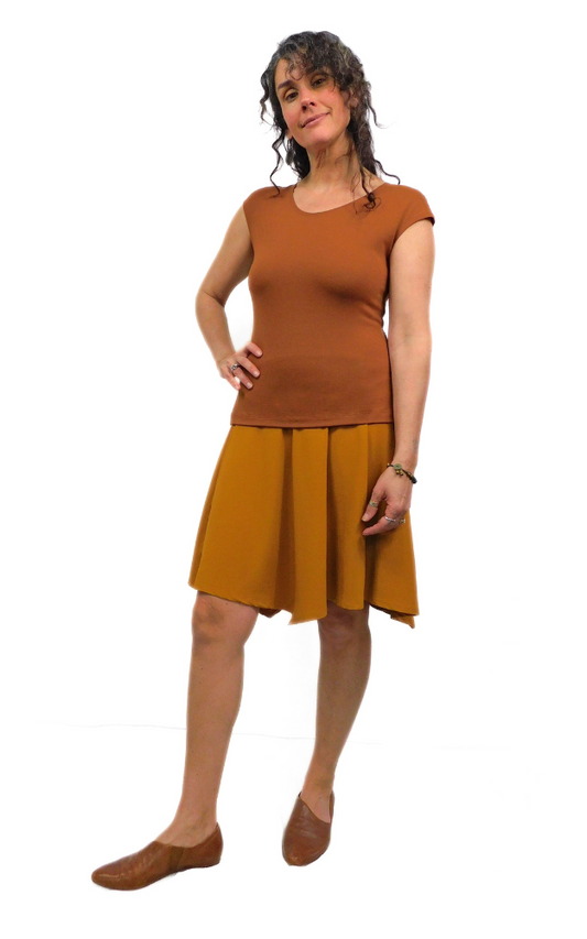 Woman standing in pose one hand on hip wearing toffee brown top and curry gold skirt