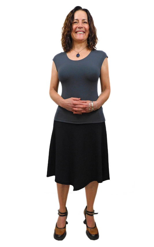 Woman standing tall with hands folded wearing graphite grey top and black skirt