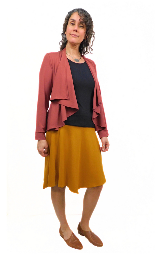 Woman standing in pose wearing black top and  curry gold skirt and wine jacket