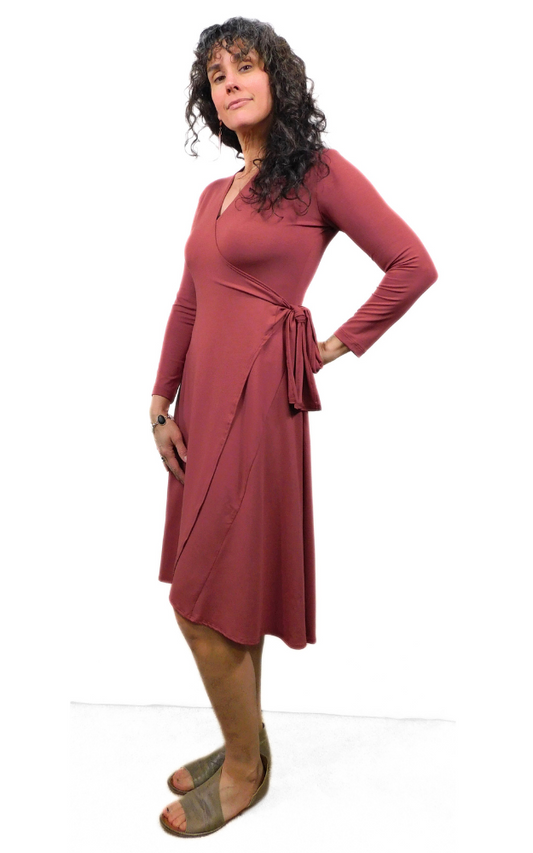 Woman standing sideways wearing wine coloured wrap dress long sleeves tie belt below knee hem