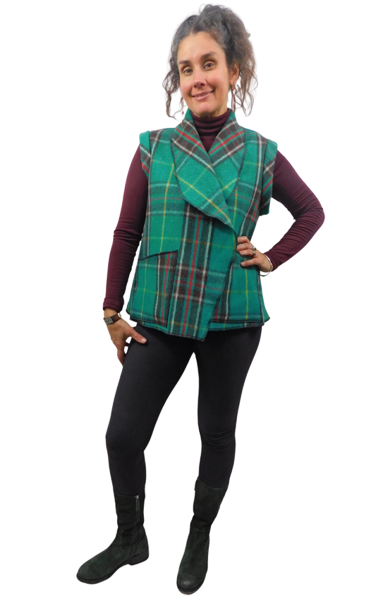Woman wearing a green and black tartan plaid vest over a wine sweater and black pants and boots.