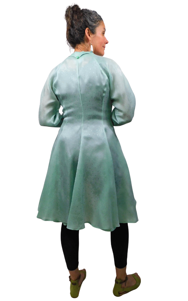 Person wearing a light green dress with long sleeves on a white background