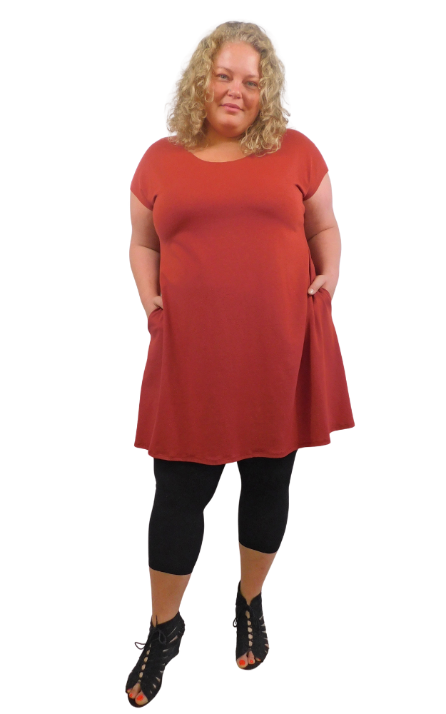 Woman wearing a red tunic and black tights and shoes with hands in pockets
