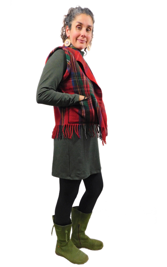 Person wearing a green dress, red tartan vest, and green boots on a white background