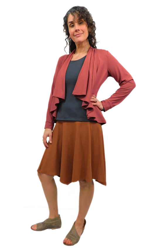 Woman standing in pose one hand on hip wearing black top and toffee brown skirt and wine jacket