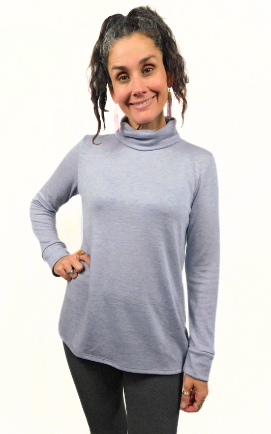 A woman wearing a heather grey cowl neck, long-sleeved merino wool and TENCEL lyocell blend sweater.
