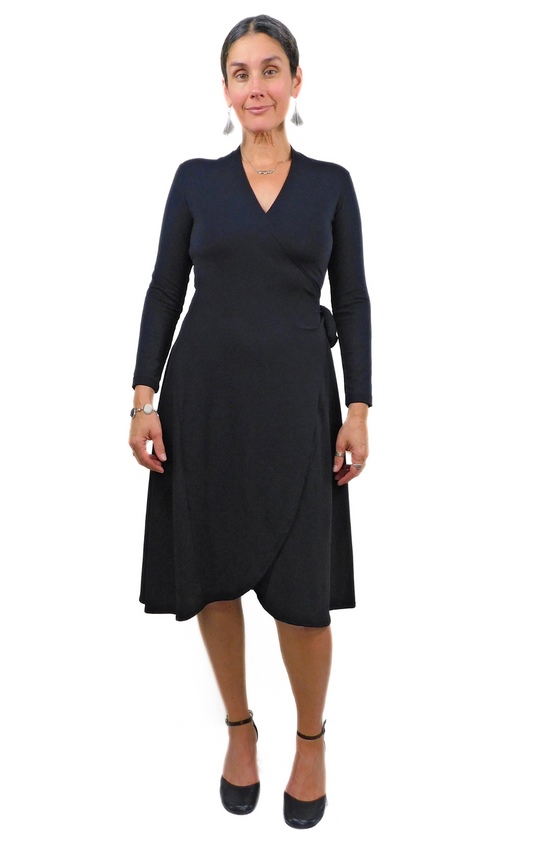 Woman standing wearing black wrap dress long sleeves tie belt below knee hem