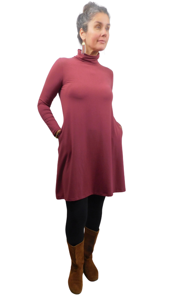 A woman modeling a long-sleeve, high-neck turtleneck tunic dress in a dusty rose wine color, styled with black leggings and brown suede boots against a plain white background.