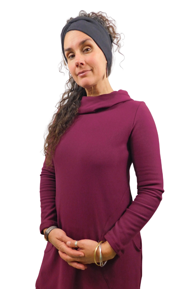 A woman modeling a long-sleeve cowl-neck tunic dress in deep burgundy, styled with a black headband against a white background.