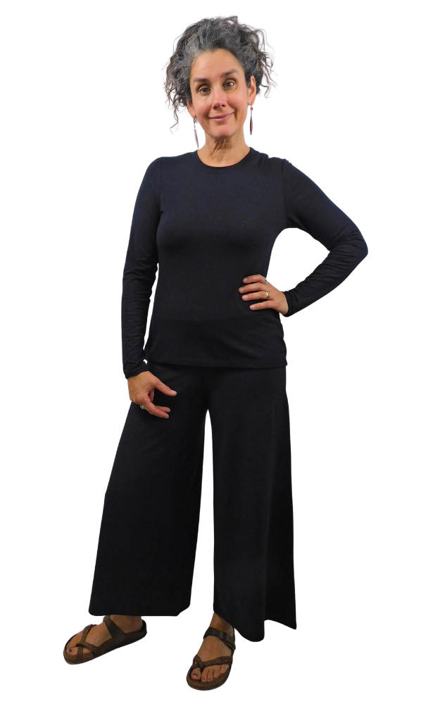 A woman modeling a black long-sleeve top and matching wide-leg pants, paired with brown sandals, against a plain white background.