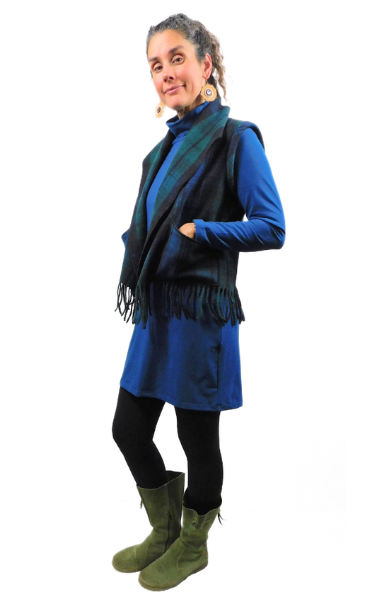 Woman wearing a blue dress, green, black and blue tartan vest, and green boots on a white background