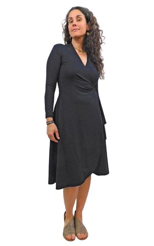 Woman standing wearing black wrap dress long sleeves tie belt below knee hem