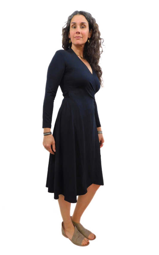 Woman standing sideways wearing black wrap dress long sleeves tie belt below knee hem