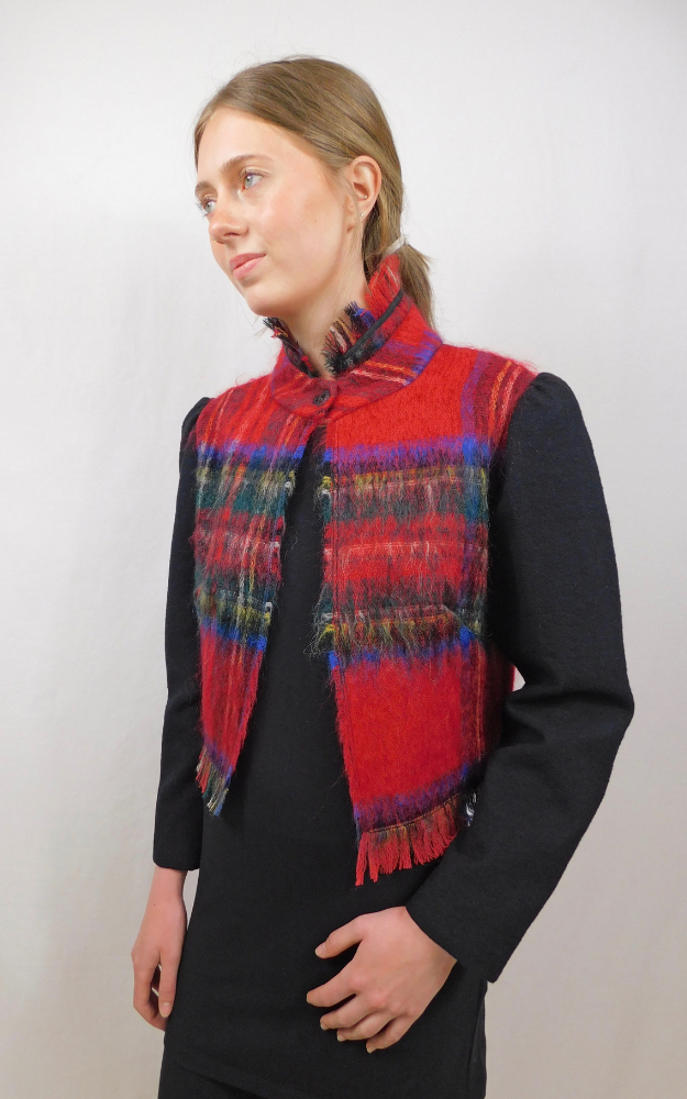 Woman wearing a red plaid jacket with collar and bottom fringe and plain long black sleeves against a white background