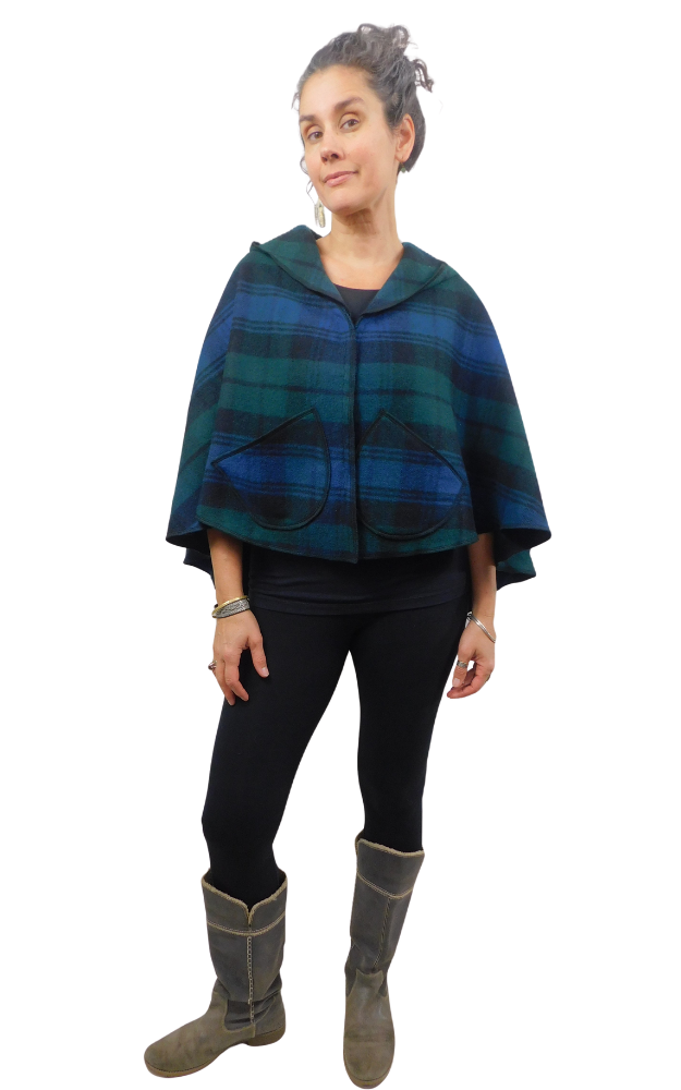 Woman wearing a blue and green and black tartan cape with front  patch pockets, over black leggings and grey boots