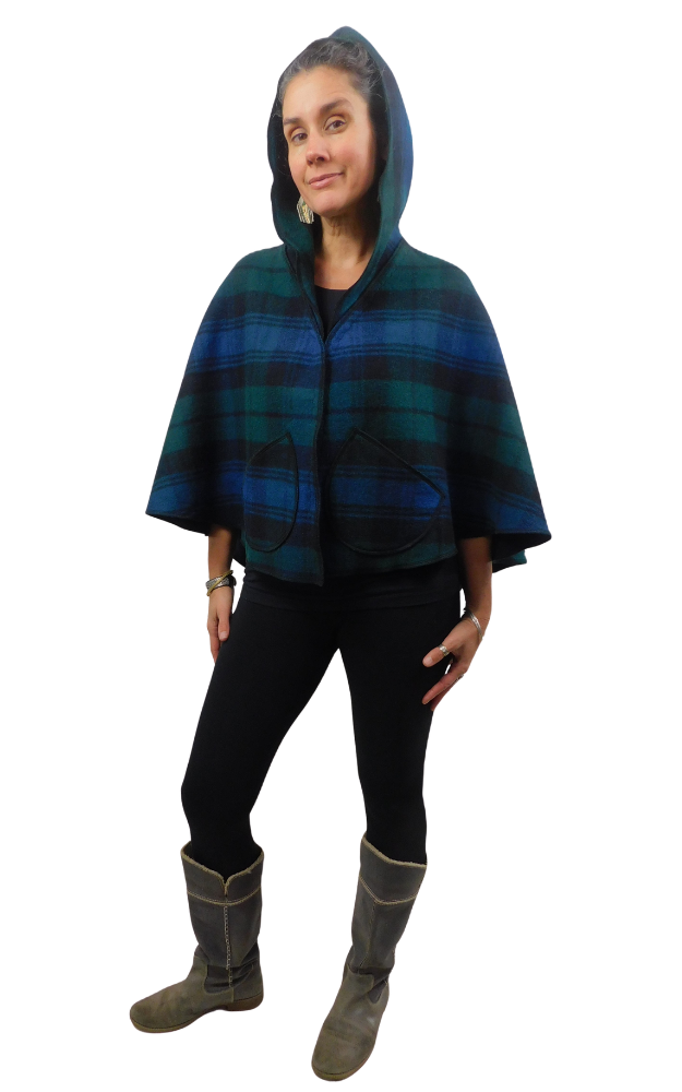 Woman wearing a blue and green and black tartan cape, worn  with hood up and front  patch pockets, over black leggings and grey boots