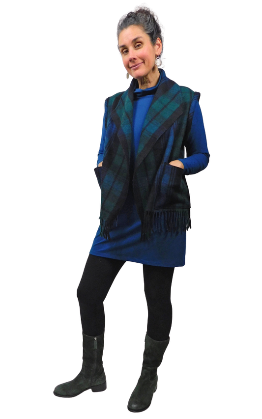 Woman wearing a blue dress, green, black and blue tartan vest, and green boots on a white background