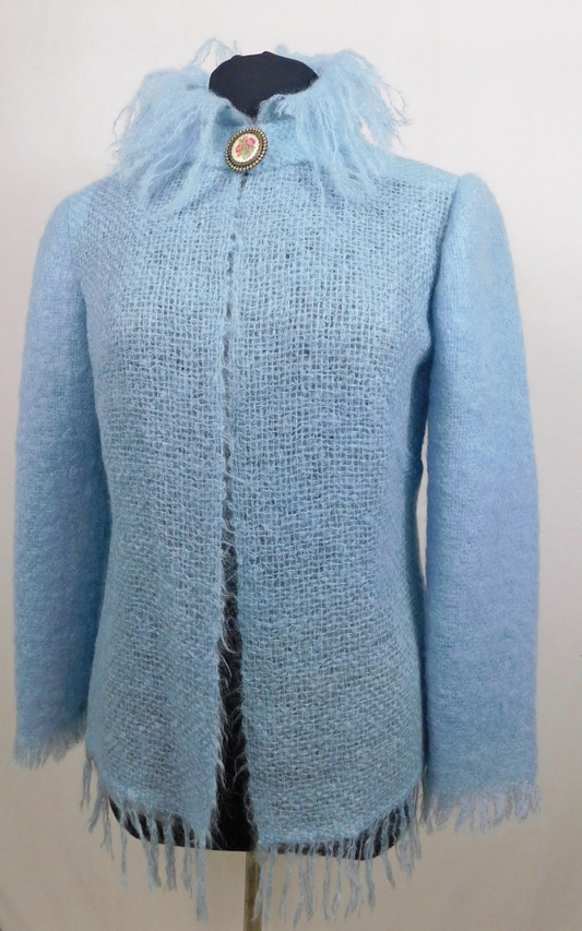 Light blue knitted coat with fringes on a mannequin against a white background