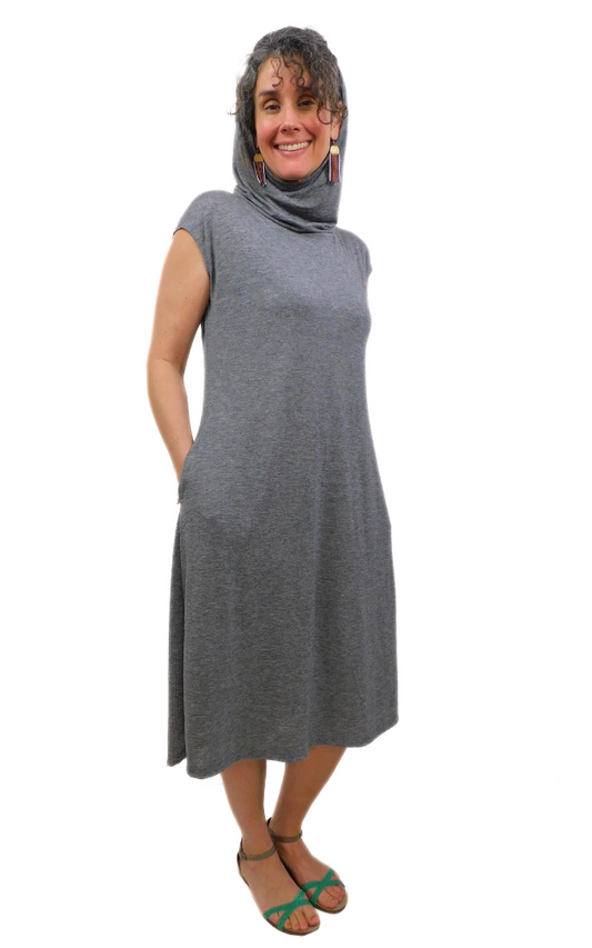 Woman standing with hands in pocket wearing lightweight charcoal tunic long dress with loose hood worn up 