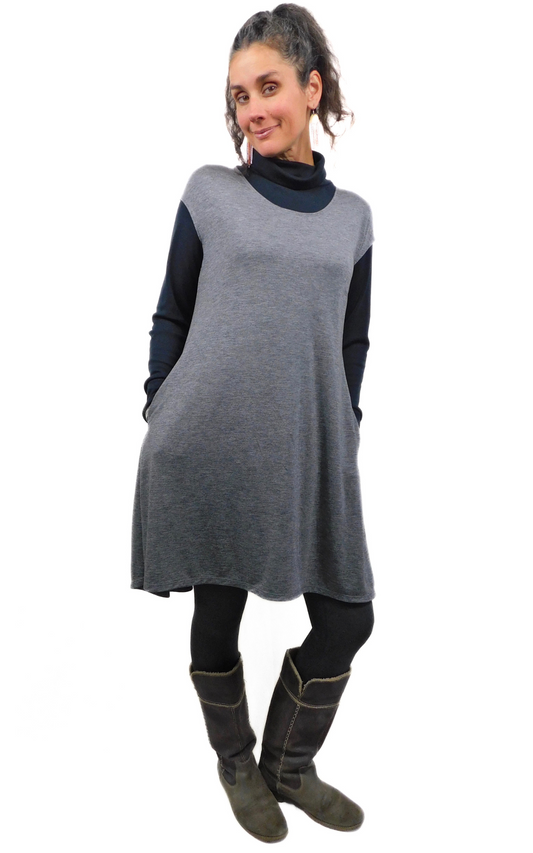 A woman wearing a gray cap-sleeve tunic dress with pockets, paired with black tights and boots.