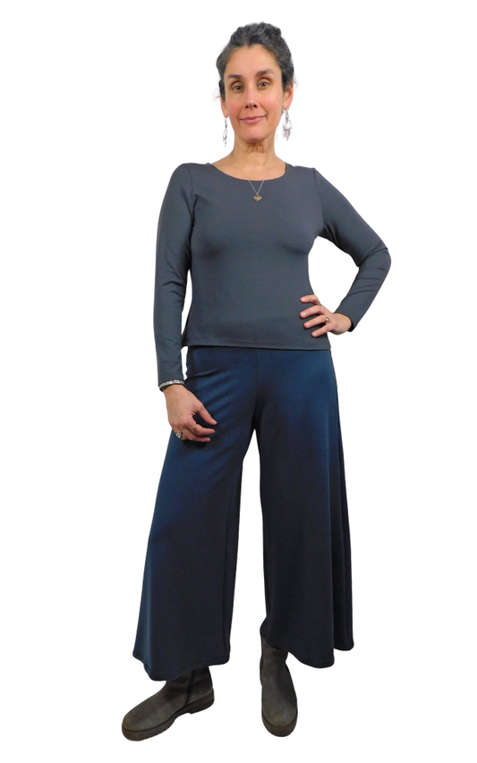 Woman wearing a gray long-sleeve top and blue wide-leg pants on a white background