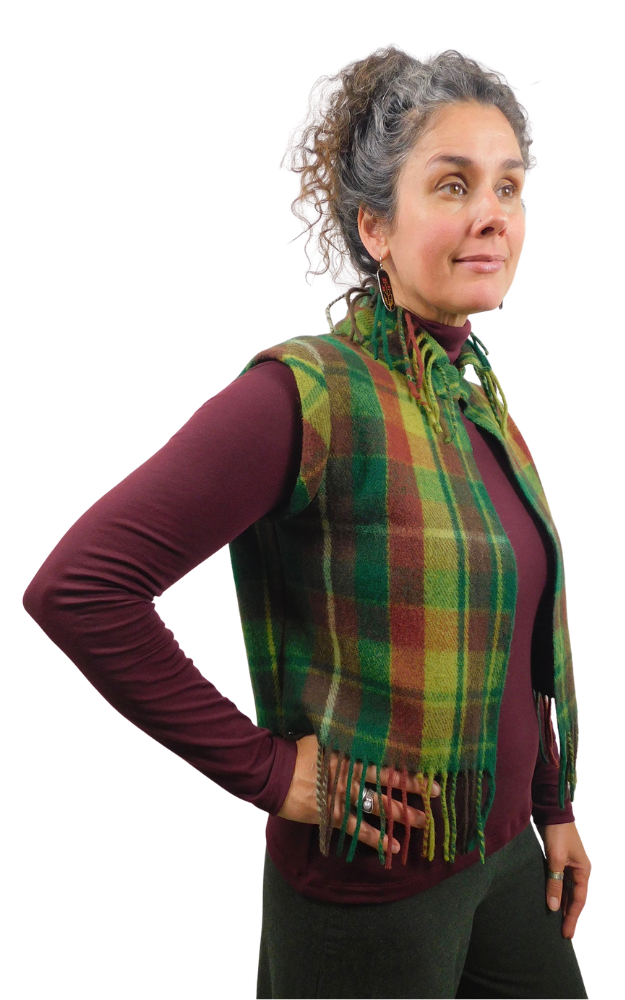 A woman modeling a green and yellow and wine tartan plaid fringed wrap vest over a burgundy long-sleeve top, set against a plain white background.
