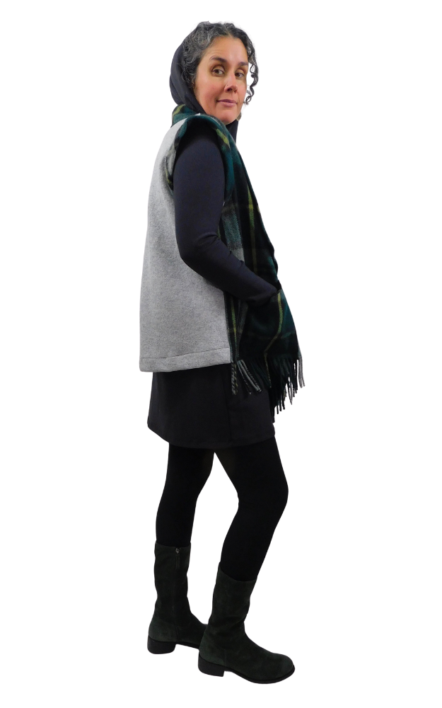 Person wearing a tartan vest with grey back, black dress, black tights, and black boots on a white background