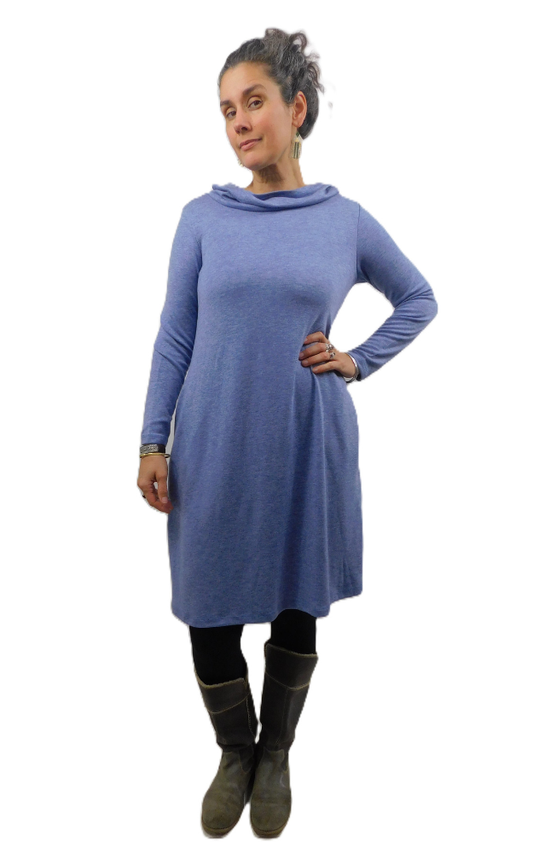 Woman wearing a long blue dress with long sleeves and cowl neck on top of black tights and grey boots