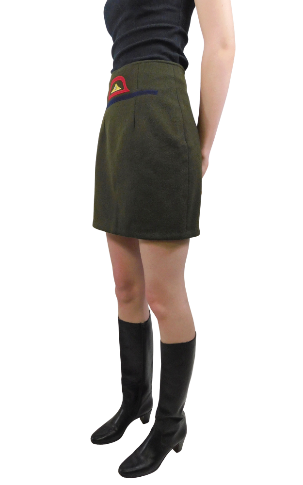 Person wearing a green skirt with a red and yellow native design and black knee-high boots on a white background