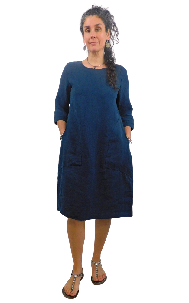 Woman wearing a blue dress with pockets  standing against a white background