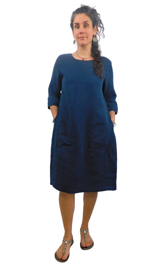 Woman wearing a blue dress with pockets  standing against a white background