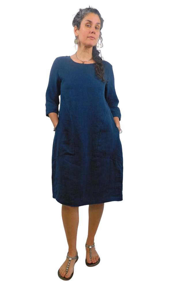 Woman wearing a blue dress with pockets  standing against a white background