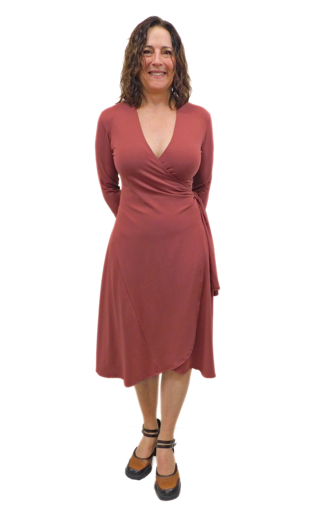 Woman standing hands behind back wearing wine coloured wrap dress long sleeves tie belt below knee hem