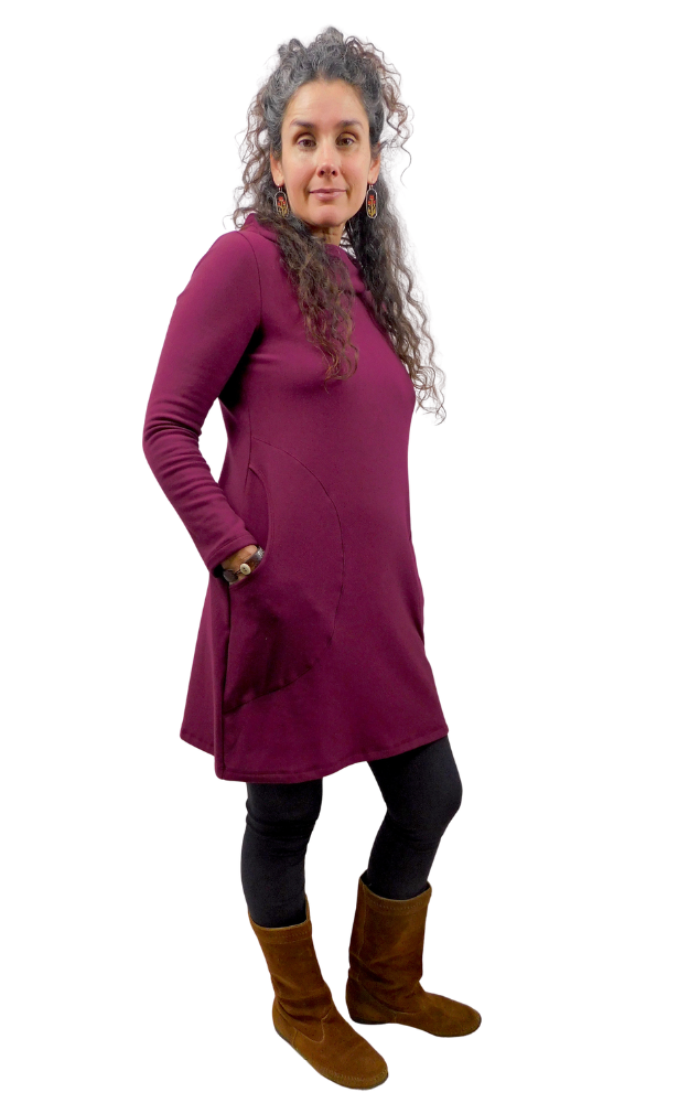 A woman modeling a long-sleeve, high-neck, knee-length tunic in deep purple whine. She is wearing black leggings and brown suede boots, standing against a solid white background.