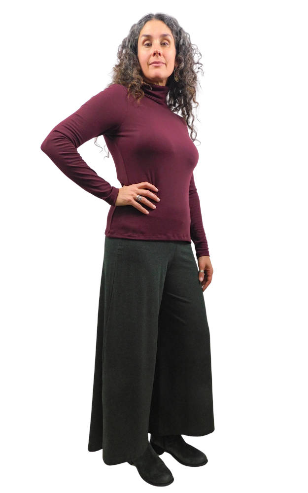 A woman modeling a long-sleeve turtleneck top in deep burgundy paired with wide-leg black pants, shown against a plain white background.