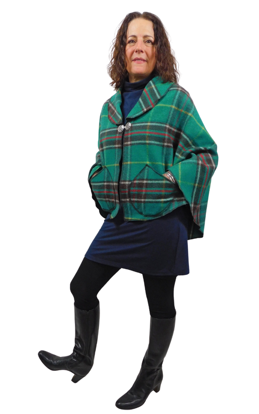 Person wearing a green plaid cape coat over a navy dress on a white background