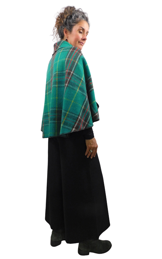 A woman wearing a green and teal tartan plaid cape over a long black dress, shown from a side-back angle against a plain white background.
