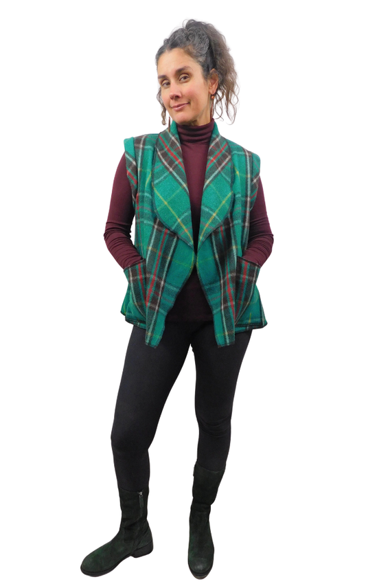 Woman wearing a green and black tartan plaid vest over a wine sweater and black pants and boots.