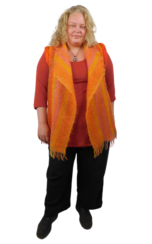 Woman wearing an orange mohair vest with fringes on top of a rust colour top and black pants against a white background