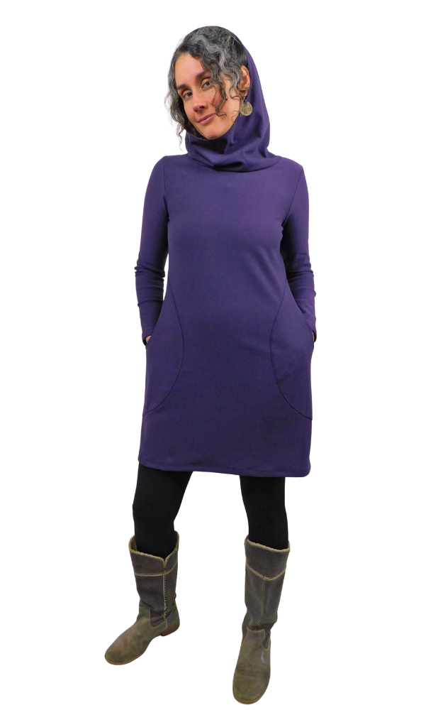 Person wearing a plum coloured tunic dress with a hood and pockets and dark boots on a white background