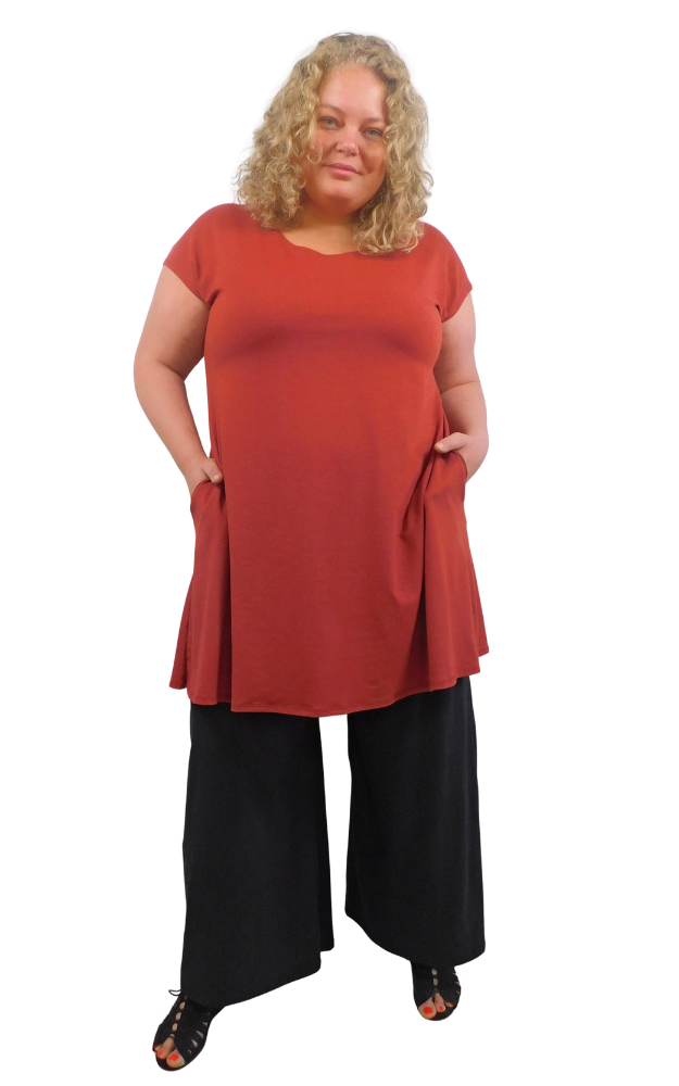 Woman wearing a red tunic with hands in pockets and long wide black pants against a white background