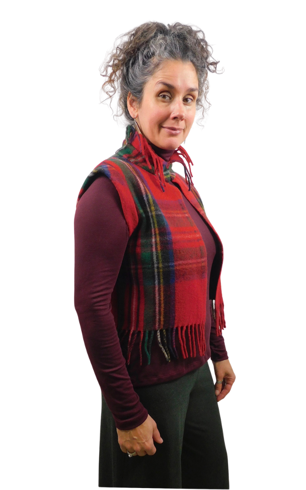 A woman modeling a red and green tartan plaid vest with fringe collar up, paired with a burgundy long-sleeve top and black pants, against a plain white background.