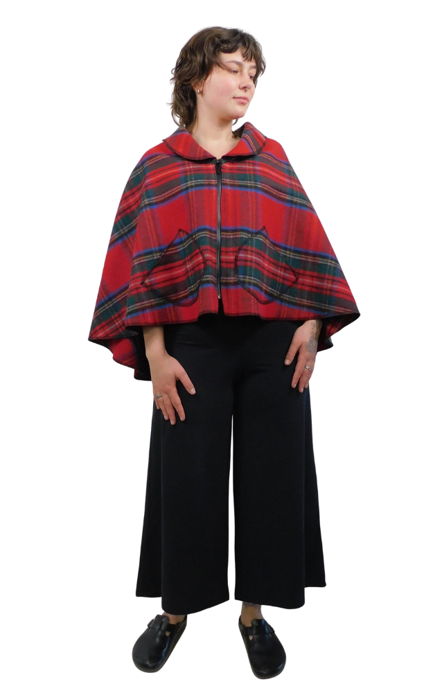 Person wearing a red and green and blue tartan plaid cape over a black outfit on a white background