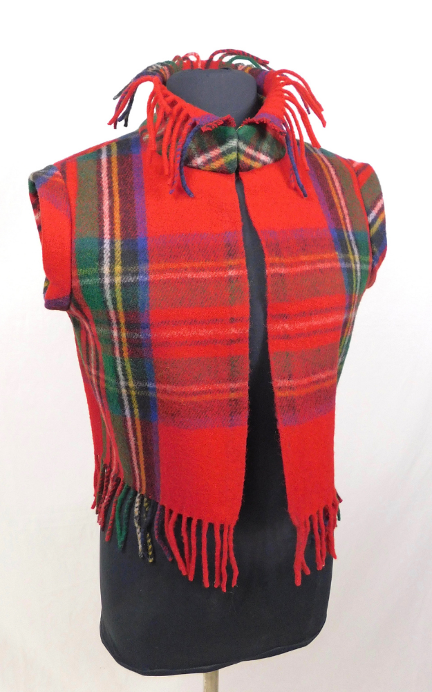 A red tartan plaid fringed vest with green, blue, and yellow stripes, displayed on a black mannequin torso against a white background.