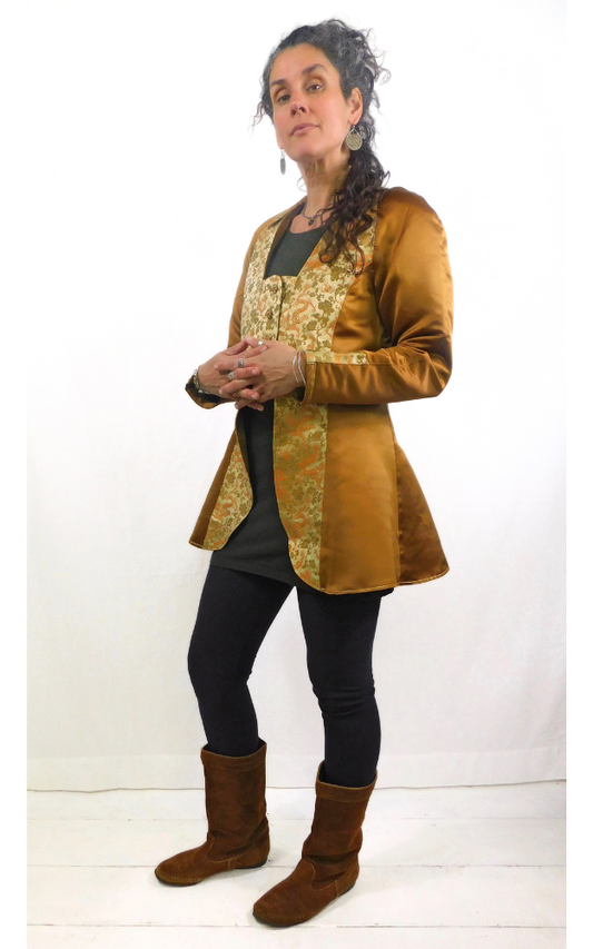 Woman wearing a bronze long vest  jacket with  gold patterned brocade front, collar and cuff, over a black outfit on a white background