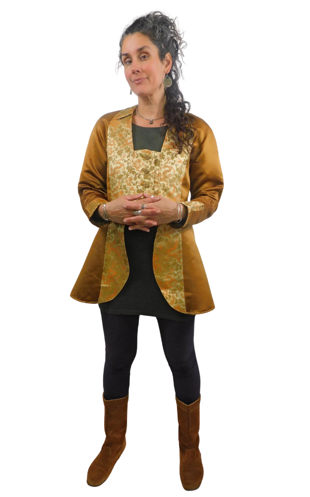 Woman with hands folded wearing a bronze long vest  jacket with  gold patterned brocade front, collar and cuff, over a black outfit on a white background